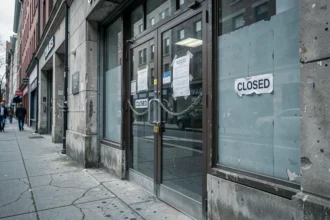 Entrée d'une agence bancaire fermée avec chaîne et cadenas sur les portes en verre, affichette de fermeture collée à la vitrine, façade urbaine négligée évoquant une faillite bancaire